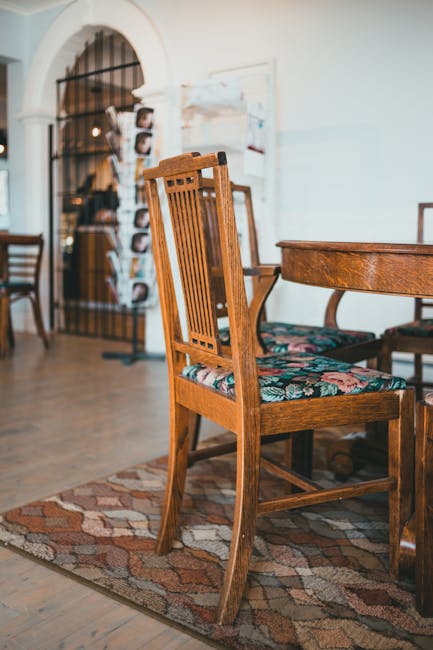 Interior view of a room in a domestic setting featuring a wooden dining chair with a floral upholstered seat positioned beside a round wooden table, both exhibiting a polished finish. The chair and ta